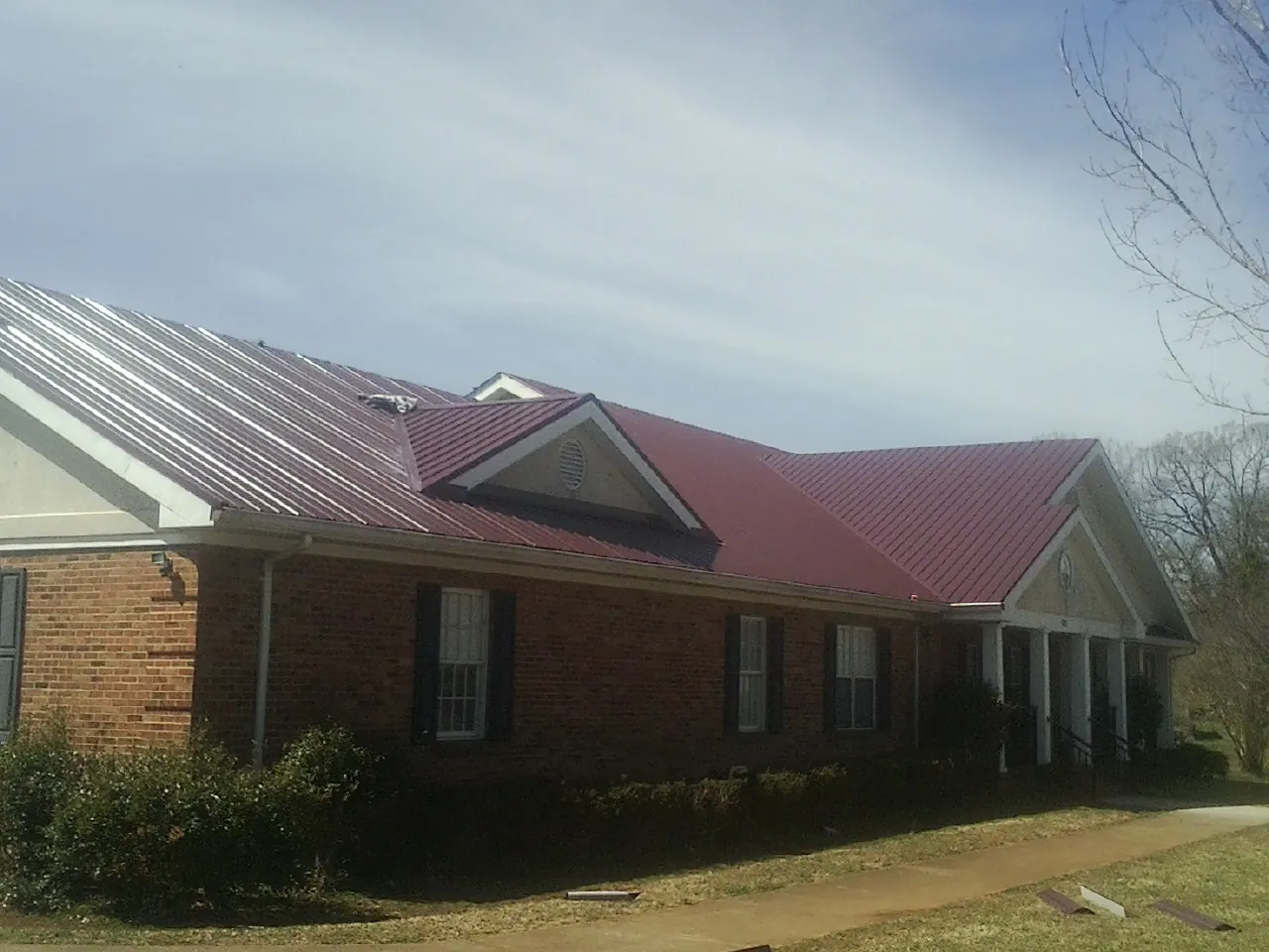 Red metal roof with gabled entries on a long brick building, from a Hail Damage Roof Repair job in Paoli